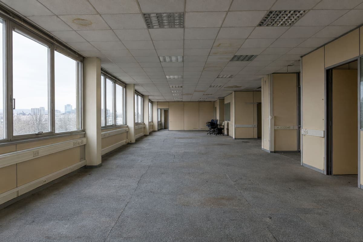 Plateau de bureaux avant travaux : moquette usée, cloisons datées et éclairage d’origine.